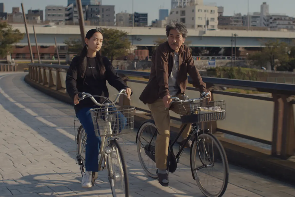 Film still from Perfect Days showing two people seated outdoors in Tokyo